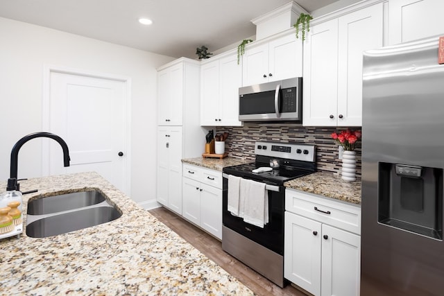 kitchen with white cabinets, stainless steel appliances, backsplash, wood finished floors, and a sink