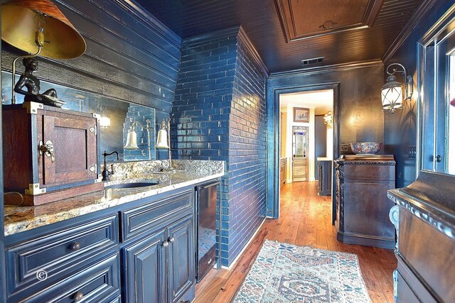 bar with light stone countertops, wood-type flooring, sink, and ornamental molding