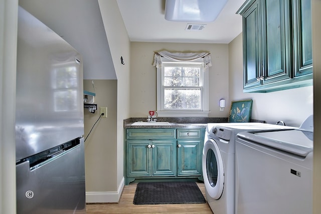 laundry area with light hardwood / wood-style floors, cabinets, independent washer and dryer, and sink