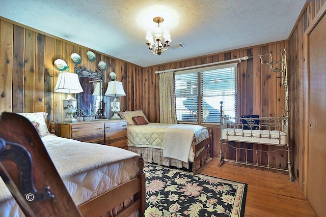 bedroom featuring wood walls, hardwood / wood-style floors, a textured ceiling, and a notable chandelier