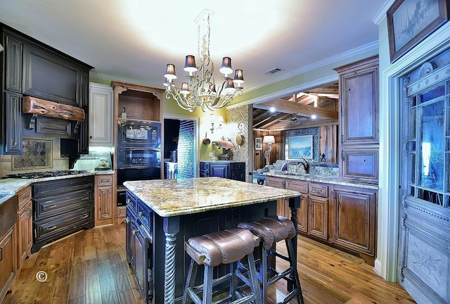 kitchen featuring hardwood / wood-style floors, ornamental molding, a notable chandelier, a kitchen island, and dark brown cabinetry