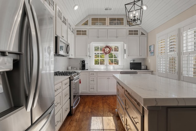 kitchen featuring white cabinets, appliances with stainless steel finishes, vaulted ceiling, and light stone countertops