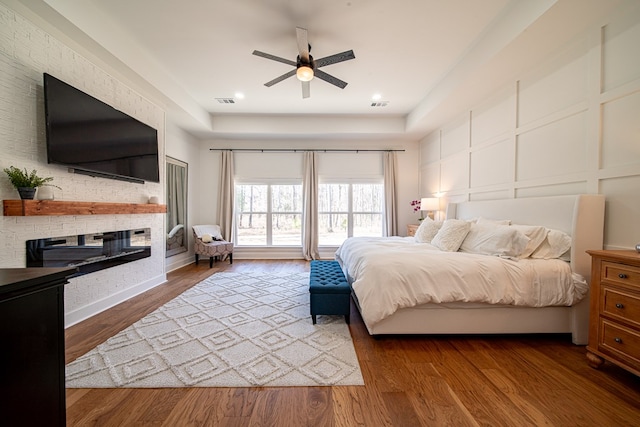 bedroom with a decorative wall, wood finished floors, visible vents, and a multi sided fireplace