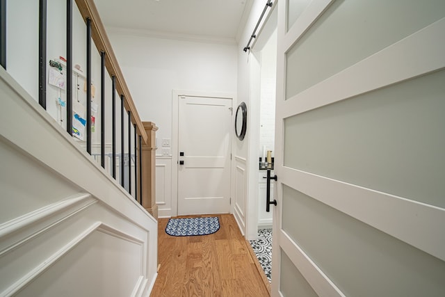 doorway to outside featuring light wood-style floors, a barn door, stairway, and crown molding