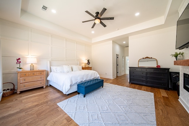 bedroom with dark wood-style floors, a tray ceiling, a glass covered fireplace, and visible vents