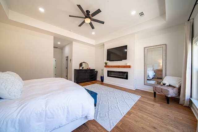 bedroom with recessed lighting, a raised ceiling, visible vents, a glass covered fireplace, and wood finished floors