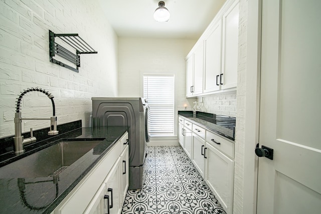 clothes washing area with light tile patterned floors, brick wall, a sink, cabinet space, and washing machine and clothes dryer