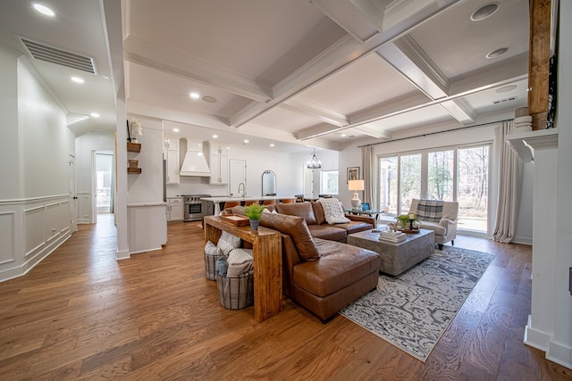 living room with a notable chandelier, visible vents, beamed ceiling, and wood finished floors