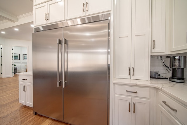 kitchen featuring light stone counters, built in refrigerator, white cabinetry, and tasteful backsplash