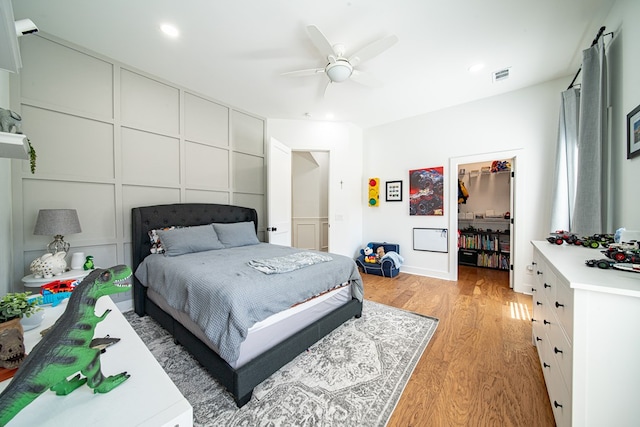 bedroom featuring ceiling fan, a decorative wall, visible vents, a spacious closet, and light wood finished floors