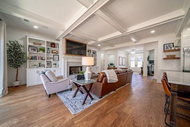 living area with french doors, a fireplace, light wood-style flooring, and beamed ceiling