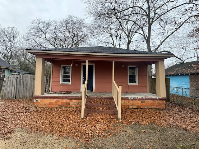 view of front of house featuring covered porch, roof with shingles, and fence