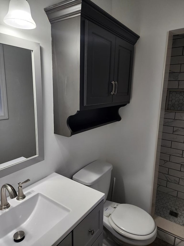 bathroom with vanity, toilet, and tiled shower