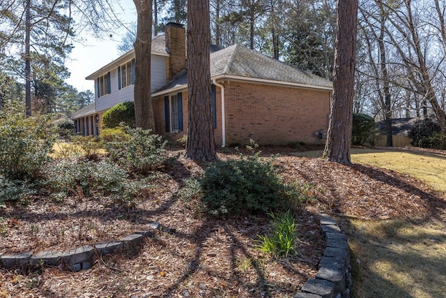 view of property exterior with brick siding, a chimney, and roof with shingles