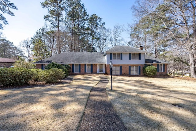 split level home with driveway, a chimney, and brick siding