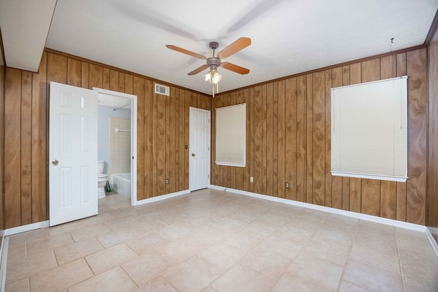 spare room featuring a ceiling fan, visible vents, wooden walls, and baseboards