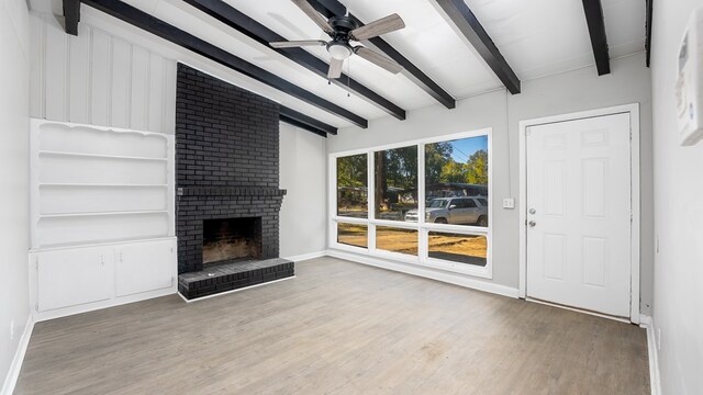 unfurnished living room with lofted ceiling with beams, ceiling fan, wood-type flooring, and a brick fireplace