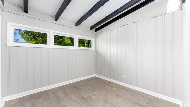 spare room featuring vaulted ceiling with beams, wood walls, and wood-type flooring