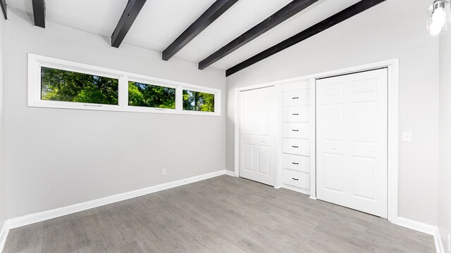 unfurnished bedroom featuring vaulted ceiling with beams and light hardwood / wood-style flooring