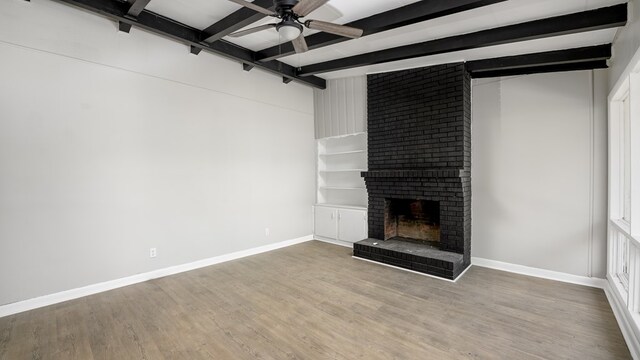 unfurnished living room featuring a brick fireplace, ceiling fan, beamed ceiling, plenty of natural light, and wood-type flooring