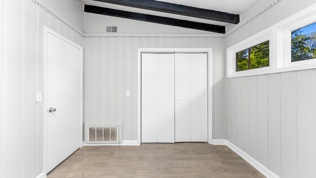 unfurnished bedroom with vaulted ceiling with beams, wooden walls, a closet, and light wood-type flooring