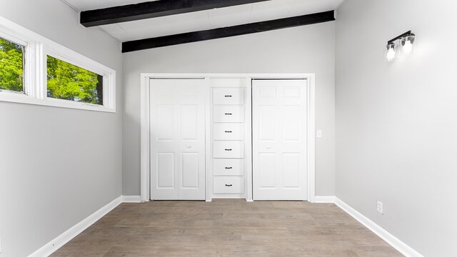 unfurnished bedroom with light wood-type flooring and vaulted ceiling with beams