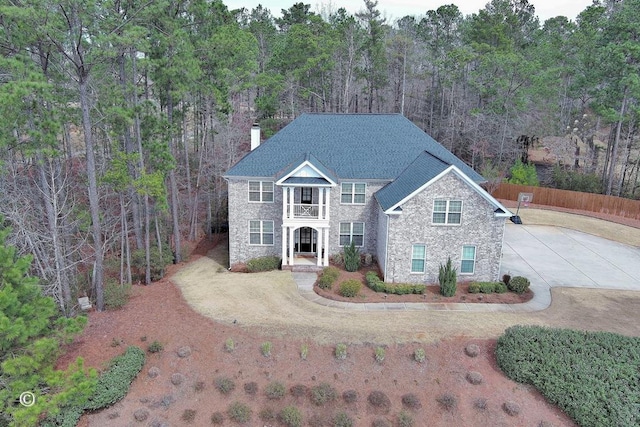 view of front of property featuring driveway, a chimney, a forest view, and fence