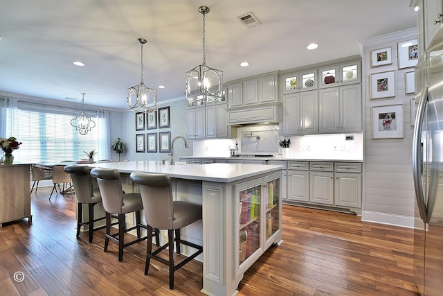 kitchen featuring a center island with sink, visible vents, glass insert cabinets, hanging light fixtures, and light countertops