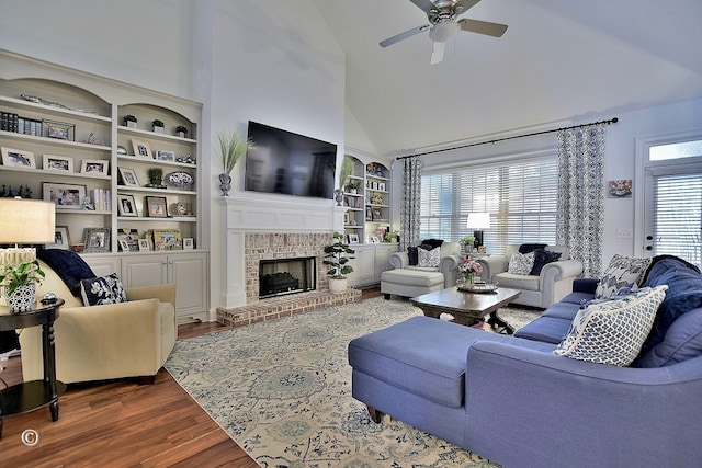 living area with built in features, ceiling fan, wood finished floors, a fireplace, and high vaulted ceiling