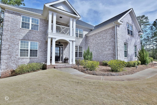 greek revival house with brick siding, a front lawn, and a balcony