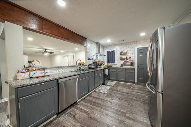 kitchen featuring dark wood-type flooring, stainless steel appliances, wall chimney range hood, kitchen peninsula, and gray cabinets