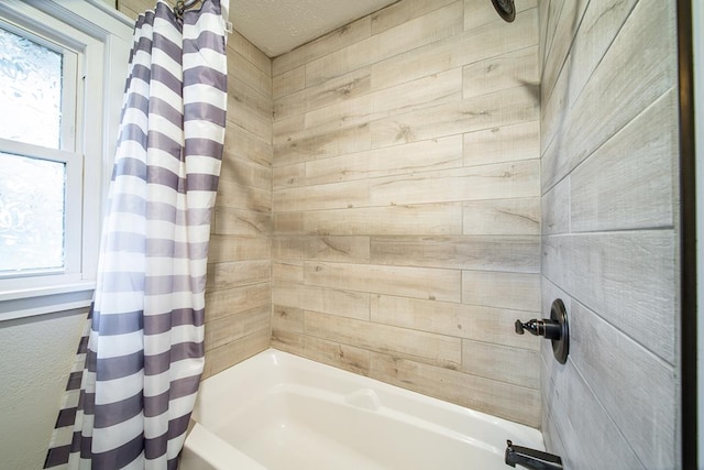 bathroom with a textured ceiling and shower / tub combo with curtain