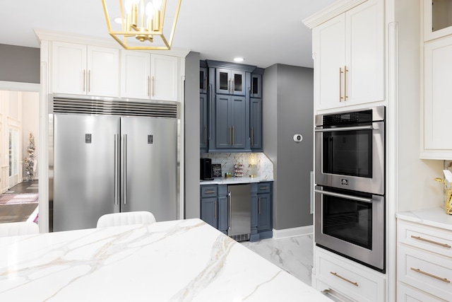 kitchen featuring light stone countertops, stainless steel appliances, a chandelier, decorative light fixtures, and decorative backsplash