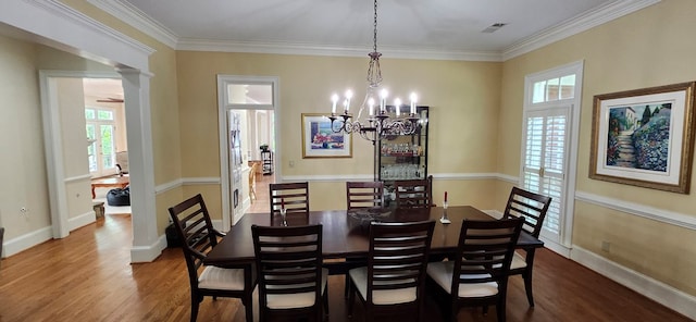 dining space with crown molding, a notable chandelier, baseboards, wood finished floors, and ornate columns