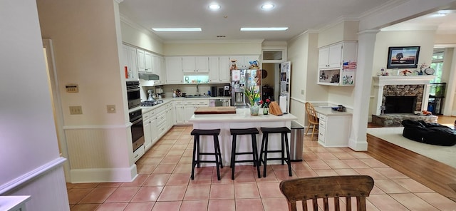 kitchen with crown molding, light countertops, under cabinet range hood, white cabinets, and stainless steel appliances