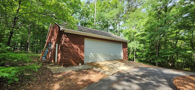 garage featuring aphalt driveway and a wooded view