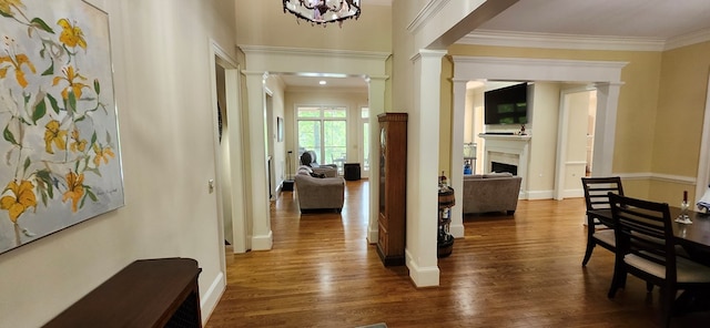 hallway featuring crown molding, ornate columns, baseboards, and wood finished floors