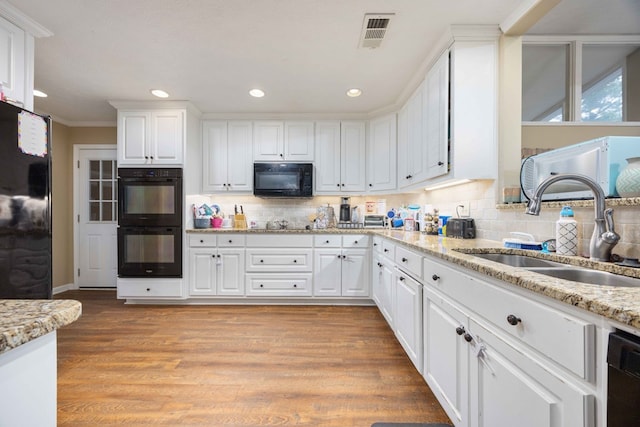 kitchen featuring a sink, white cabinetry, decorative backsplash, visible vents, and black appliances