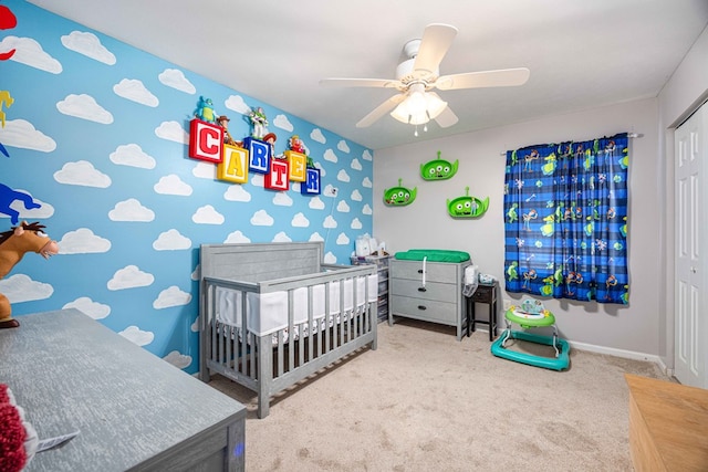 bedroom featuring a ceiling fan, a crib, baseboards, a closet, and carpet flooring