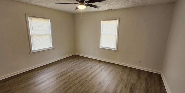 empty room featuring a ceiling fan, visible vents, dark wood-style floors, baseboards, and a textured ceiling