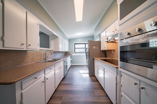 kitchen with dark wood-type flooring, under cabinet range hood, lofted ceiling, stainless steel appliances, and a sink