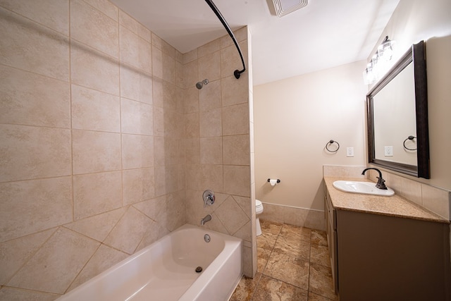 bathroom featuring visible vents, toilet, stone tile flooring, washtub / shower combination, and vanity