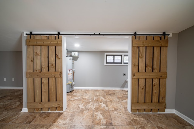 below grade area featuring stone finish floor, baseboards, gas water heater, and a barn door