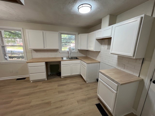 3015 Walker St, Columbus, GA 31903 - kitchen with a textured ceiling, wooden counters, light wood finished floors, white cabinetry, and backsplash