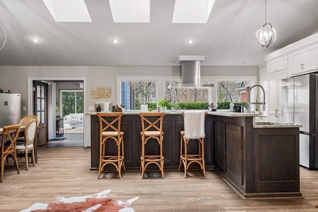 kitchen featuring light wood finished floors, a skylight, freestanding refrigerator, island range hood, and a sink