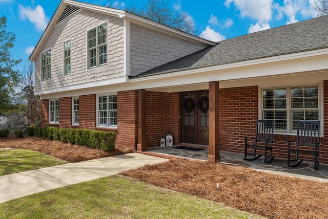 view of front facade with brick siding, covered porch, and roof with shingles