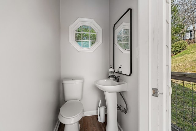 half bathroom featuring toilet, wood finished floors, baseboards, and a sink