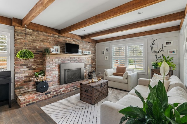 living area with beam ceiling, a brick fireplace, and wood finished floors