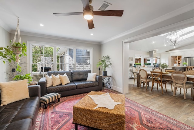 living area featuring light wood-type flooring, visible vents, ceiling fan with notable chandelier, recessed lighting, and crown molding