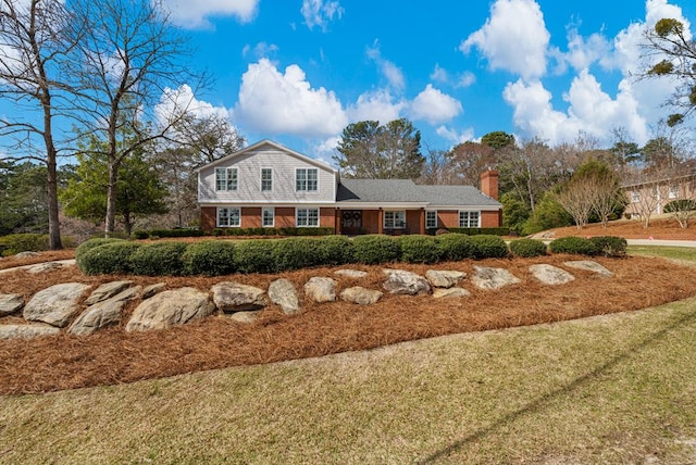 view of front of property with brick siding, a front lawn, and a chimney